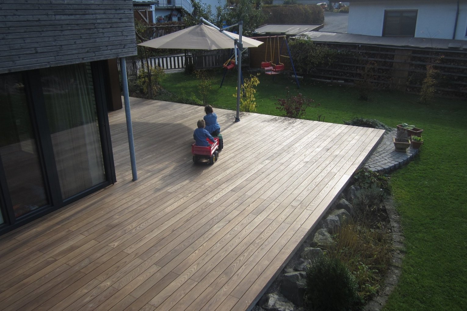 Terrasse aus Thermoahorn Zwei Kinder spielen auf einer großen Holzterrasse aus Thermoahorn.