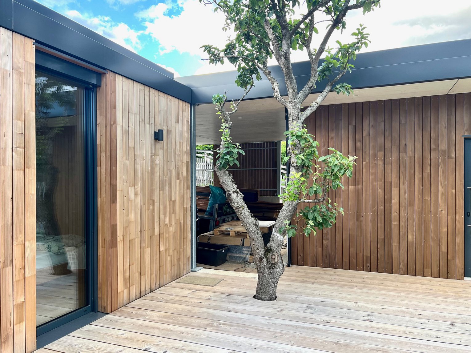 SWERO Fassade Ein modernes Haus mit Holzfassade und Holzterrasse und einem Baum davor