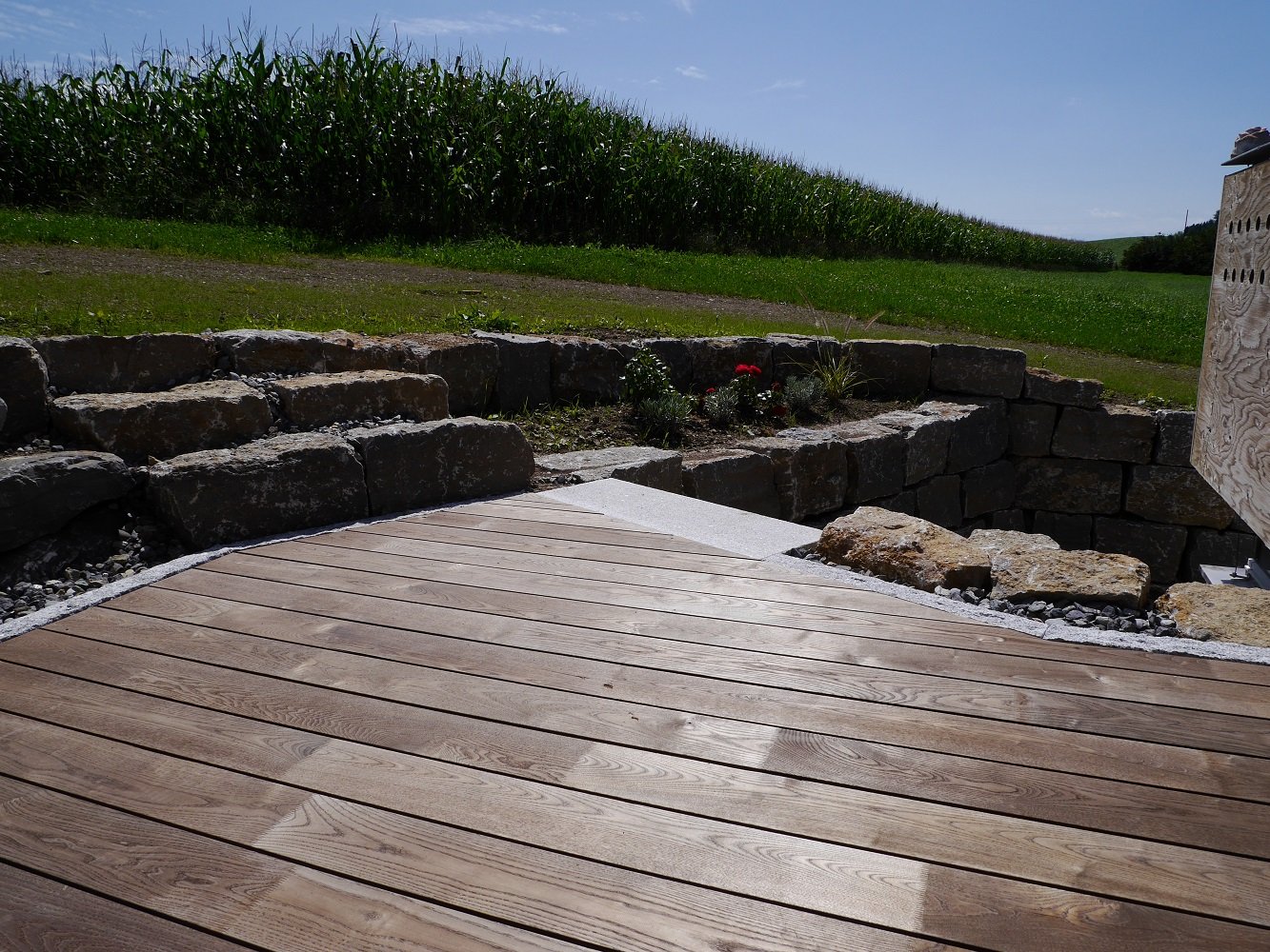 Terrasse aus Holzdielen mit einer Wiese im Hintergrund.