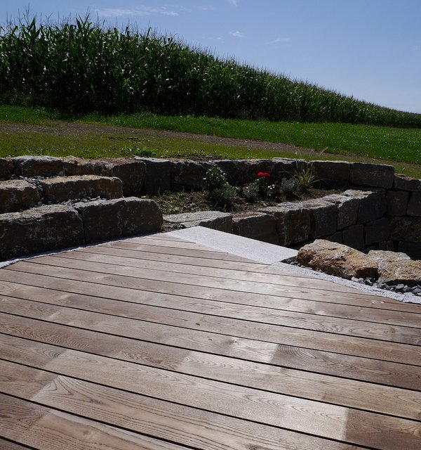 Terrasse aus Holzdielen mit einer Wiese im Hintergrund.