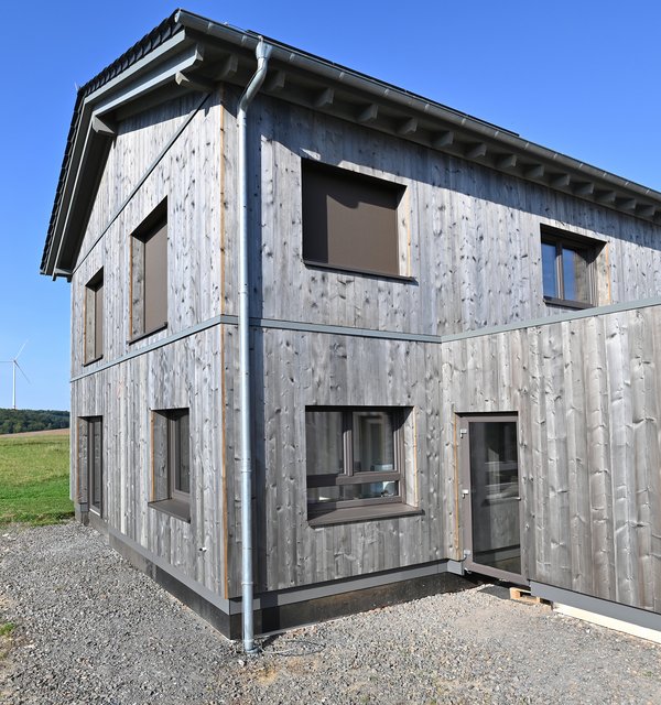 Wohnhaus mit grauer Holzfassade in ländlicher Gegend. 